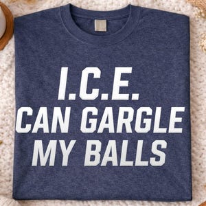 May include: Heather navy blue t-shirt with the text "I.C.E. CAN GARGLE MY BALLS" in white block letters. The shirt is displayed on a white, textured surface with a mug of hot chocolate and dried oranges.