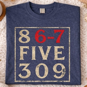 Może przedstawiać: Granatowa koszulka z postarzaną kwadratową grafiką. Grafika zawiera czerwone cyfry "8 6-7" oraz słowa "FIVE 309" w stylu vintage. Koszulka jest prezentowana na przytulnej, teksturowanej powierzchni.