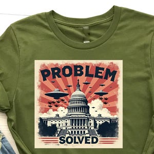 Könnte beinhalten: Olivgrünes T-Shirt mit einem Grafikdesign, das das US-Kapitol, UFOs und die Worte "PROBLEM SOLVED" in einem Vintage-Stil zeigt. Das Shirt wird mit blauen Jeans und braunen Stiefeletten kombiniert.