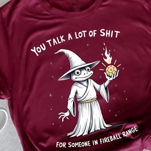 Funny fantasy humor t-shirt featuring a frog-themed design paired with the phrase “You Talk a Lot of Shit for Someone in Fireball Range.” This graphic tee blends sarcastic humor with a playful fantasy reference, creating a bold and eye-catching statement. Ideal for fans of memes, tabletop humor, and exaggerated fantasy jokes. Designed for casual daily wear with a comfortable unisex fit, perfect for relaxed outings, game nights, or expressive everyday outfits.