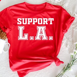 以下が含まれることがあります： 「SUPPORT L.A.」という白い文字が書かれた赤いTシャツ