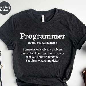 Puede incluir: Camiseta gris oscuro jaspeado con la palabra "Programmer" en blanco y una definici&oacute;n. La definici&oacute;n dice: "Alguien que resuelve un problema que no sab&iacute;as que ten&iacute;as, de una manera que no entiendes."