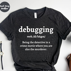 May include: Dark grey heather t-shirt with the word "debugging" in white, along with a definition. The definition reads: "Being the detective in a crime movie where you are also the murderer."