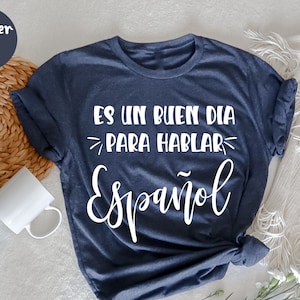 May include: A navy blue t-shirt with white text that reads "Es un buen dia para hablar Espanol".
