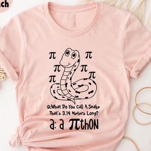Puede incluir: Camiseta color melocotón claro con un diseño de serpiente negra y el texto "Q: What Do You Call A Snake That's 3.14 Metros Long? a: a πthon". La camiseta tiene mangas enrolladas.