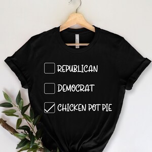 May include: Black t-shirt with white text. The text includes three check boxes with the words "Republican", "Democrat", and "Chicken Pot Pie". The "Chicken Pot Pie" box is checked.