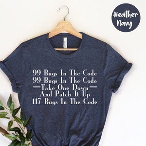 Op de afbeelding: Heather navy t-shirt met de witte tekst "99 Bugs In The Code, Take One Down, And Patch It Up, 117 Bugs In The Code". Het shirt wordt gepresenteerd op een houten hanger.