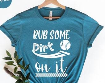 Op de afbeelding: Een turquoise T-shirt met de tekst "RUB SOME DIRT ON IT" in wit. Een witte honkbal bevindt zich boven het woord "DIRT" en een witte pijl onder het woord "IT".