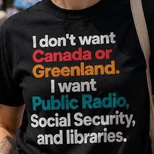 May include: A black short-sleeved t-shirt featuring the text: I don't want Canada or Greenland. I want Public Radio, Social Security, and libraries. The words Canada, Greenland, Public Radio, and Social Security are printed in different colors.