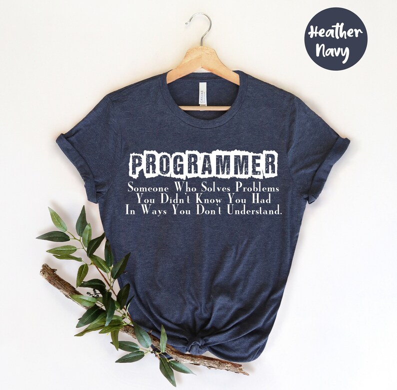Puede incluir: Camiseta azul marino con la palabra "PROGRAMMER" en blanco. Debajo, el texto dice: "Alguien que resuelve problemas que no sab&iacute;as que ten&iacute;as de maneras que no entiendes."