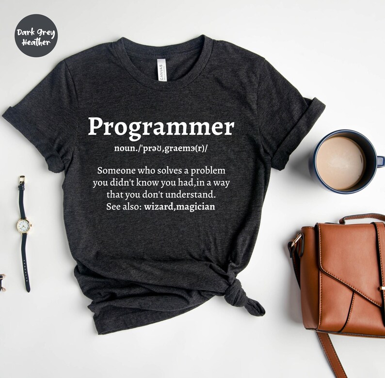 Puede incluir: Camiseta gris oscuro jaspeado con la palabra "Programmer" en blanco y una definici&oacute;n. La definici&oacute;n dice: "Alguien que resuelve un problema que no sab&iacute;as que ten&iacute;as, de una manera que no entiendes."