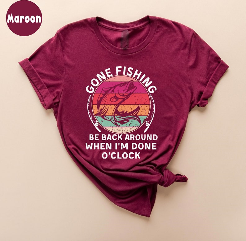 May include: Maroon t-shirt with the text "GONE FISHING" above a graphic of a fish jumping out of the water. Below the graphic, the text reads "BE BACK AROUND WHEN I'M DONE O'CLOCK".