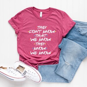 May include: A pink t-shirt with the text "They don't know that we know they know we know" in white with colorful dots.