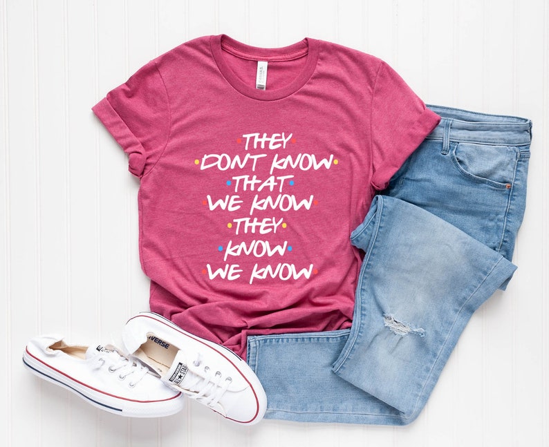 May include: A pink t-shirt with the text "They don't know that we know they know we know" in white with colorful dots.