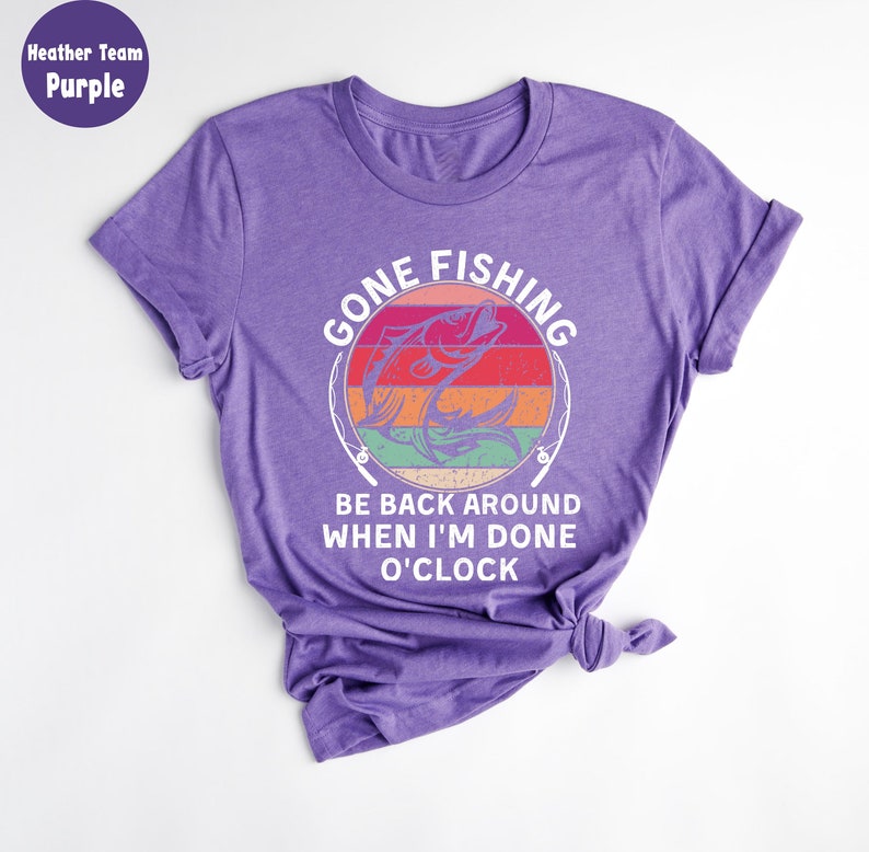May include: Purple t-shirt with the text "GONE FISHING" above a graphic of a fish jumping out of the water. The text "BE BACK AROUND WHEN I'M DONE O'CLOCK" is below the graphic. The shirt is knotted at the bottom.