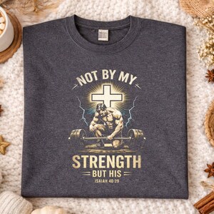 K&ouml;nnte beinhalten: Dunkelgraues meliertes T-Shirt mit einer Grafik mit einem Kreuz, einem Gewichtheber und dem Text "NOT BY MY STRENGTH BUT HIS Isaiah 40:29". Das Shirt hat einen Rundhalsausschnitt.