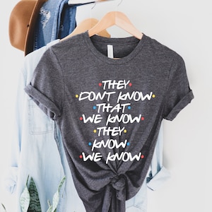 May include: A dark grey t-shirt with the text "They don't know that we know. They know we know." printed in white with colorful dots.