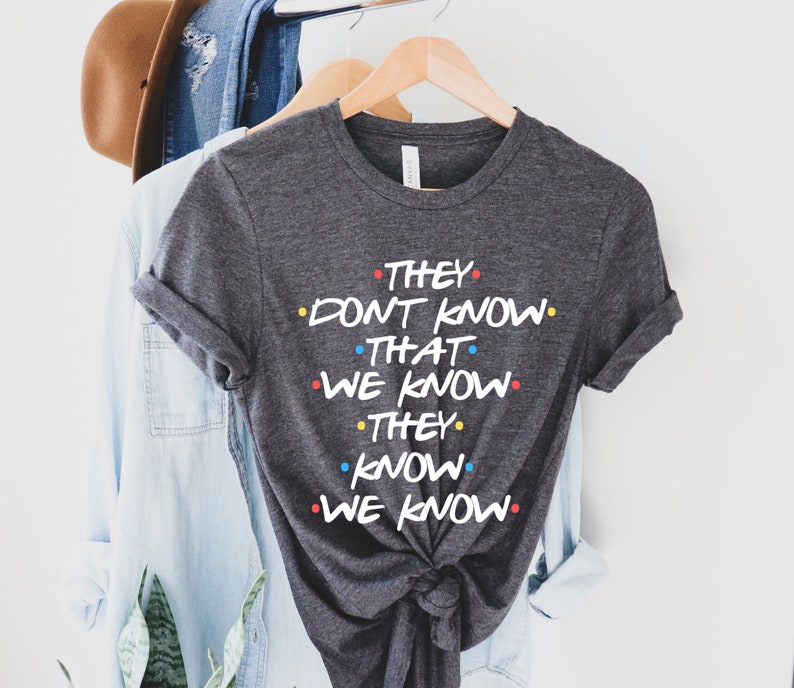 May include: A dark grey t-shirt with the text "They don't know that we know. They know we know." printed in white with colorful dots.