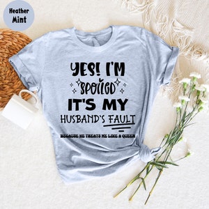 May include: A heather mint t-shirt with the text "YES! I'M SPOILED IT'S MY HUSBAND'S FAULT BECAUSE HE TREATS ME LIKE A QUEEN" printed in black.