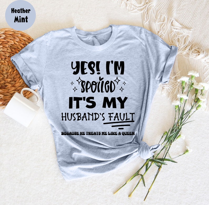 May include: A heather mint t-shirt with the text "YES! I'M SPOILED IT'S MY HUSBAND'S FAULT BECAUSE HE TREATS ME LIKE A QUEEN" printed in black.