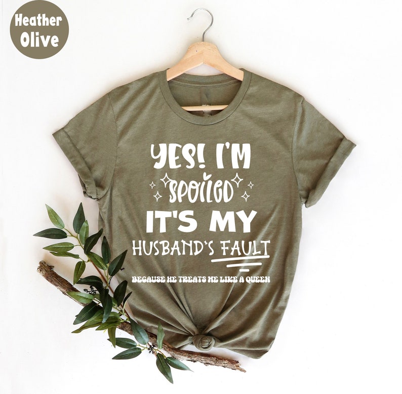 May include: A green t-shirt with the text "YES! I'M SPOILED IT'S MY HUSBAND'S FAULT BECAUSE HE TREATS ME LIKE A QUEEN" in white.