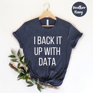 Op de afbeelding: Marineblauw t-shirt met de witte tekst "I BACK IT UP WITH DATA". Het t-shirt hangt aan een houten hanger, met een takje groen links. De woorden "Heather Navy" staan in een cirkel rechtsboven.
