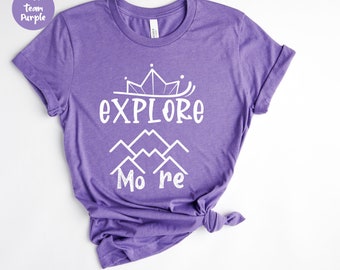 Könnte beinhalten: Ein meliertes lila T-Shirt mit dem weißen Schriftzug "EXPLORE More", einer Krone und einem Bergmotiv. Das T-Shirt ist aus weichem Material und hat kurze Ärmel.