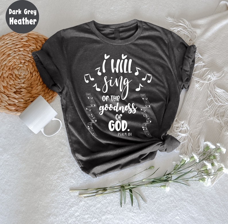 K&ouml;nnte beinhalten: Dunkelgraues Melange-T-Shirt mit dem wei&szlig;en Text "I will sing of the goodness of God", Noten und Notenlinien. Der Text "Psalm 89:1" ist darunter gedruckt. Das T-Shirt ist am unteren Ende geknotet.
