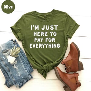 K&ouml;nnte beinhalten: Olivengr&uuml;nes T-Shirt mit dem Text "I'm just here to pay for everything" in Wei&szlig;.