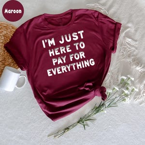 K&ouml;nnte beinhalten: Ein T-Shirt in der Farbe Weinrot mit dem Aufdruck "I'm just here to pay for everything" in Wei&szlig;.
