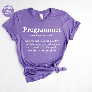 Puede incluir: Una camiseta morada con la palabra "Programador" en blanco y una definici&oacute;n. La definici&oacute;n dice: "Alguien que resuelve un problema que no sab&iacute;as que ten&iacute;as, de una manera que no entiendes."