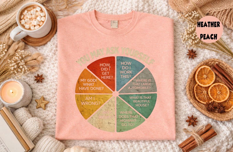 Puede incluir: Camiseta melocot&oacute;n con un dise&ntilde;o de diagrama circular y la frase "YOU MAY ASK YOURSELF". El diagrama incluye preguntas como "&iquest;C&oacute;mo llegu&eacute; aqu&iacute;?" y "&iquest;D&oacute;nde est&aacute; ese coche grande?"