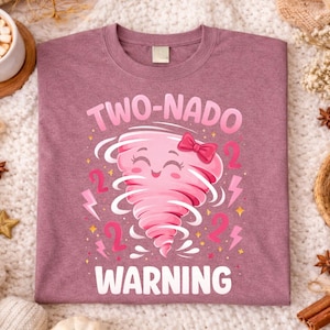 Op de afbeelding: Mauvekleurig T-shirt met een afbeelding van een roze tornado met een strik, het nummer 2 en bliksemschichten. De tekst luidt "TWO-NADO WARNING". Het shirt ligt op een witte, getextureerde ondergrond.