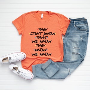 May include: Orange t-shirt with the text "They don't know that we know they know we know" in black with colorful dots.
