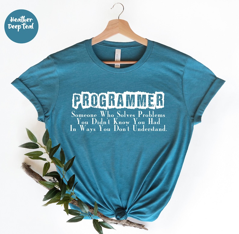 Puede incluir: Una camiseta de color verde azulado con el texto "PROGRAMMER" en letras blancas. Debajo de la palabra "PROGRAMMER" est&aacute; el texto: "Someone Who Solves Problems You Didn't Know You Had In Ways You Don't Understand."