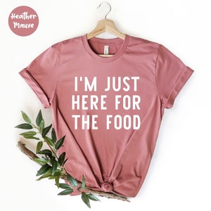 Puede incluir: Una camiseta de color malva con el texto "I'm just here for the food" impreso en blanco.