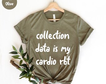 Puede incluir: Camiseta verde oliva con el texto blanco "collection data is my cardio rbt". La camiseta está colgada de una percha de madera. Una ramita de vegetación se coloca en la parte inferior izquierda de la camiseta.
