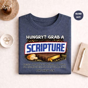 May include: Heather navy blue t-shirt with the text "HUNGRY? GRAB A SCRIPTURE" above an illustration of a book and bread. The shirt also features the text "BLESSED ARE THOSE WHO HUNGER AND THIRST FOR RIGHTEOUSNESS, FOR THEY WILL BE FILLED MATTHEW 5:6".