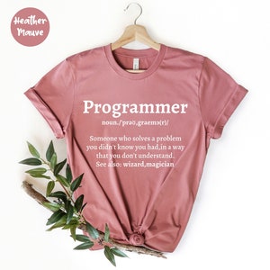 Puede incluir: Camiseta color malva con la palabra "Programmer" en blanco y una definici&oacute;n. La definici&oacute;n dice: "Alguien que resuelve un problema que no sab&iacute;as que ten&iacute;as, de una manera que no entiendes."