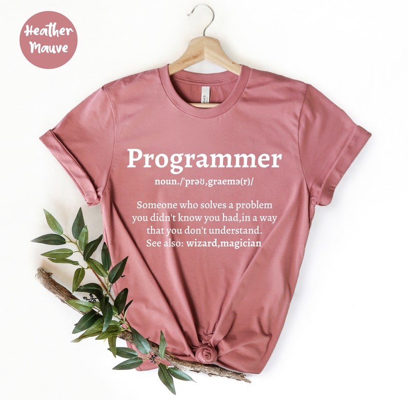 Puede incluir: Camiseta color malva con la palabra "Programmer" en blanco y una definici&oacute;n. La definici&oacute;n dice: "Alguien que resuelve un problema que no sab&iacute;as que ten&iacute;as, de una manera que no entiendes."