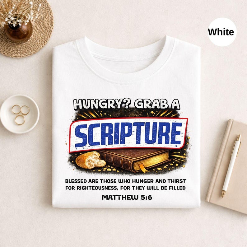 May include: White t-shirt with the text "HUNGRY? GRAB A SCRIPTURE" in a red and blue design. Below the text is an illustration of a loaf of bread and a closed book. The text "BLESSED ARE THOSE WHO HUNGER AND THIRST FOR RIGHTEOUSNESS, FOR THEY WILL BE FILLED MATTHEW 5:6" is printed below the illustration.