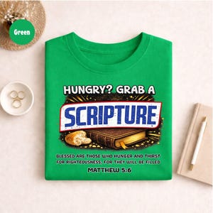 May include: A bright green t-shirt with the text "HUNGRY? GRAB A SCRIPTURE" in a bold, stylized font. Below the text is an illustration of a book and bread. The shirt also includes the Bible verse Matthew 5:6.