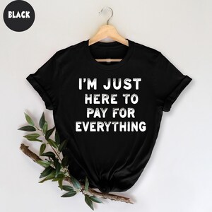 K&ouml;nnte beinhalten: Schwarzes T-Shirt mit dem Text "I'm just here to pay for everything" in Wei&szlig;.