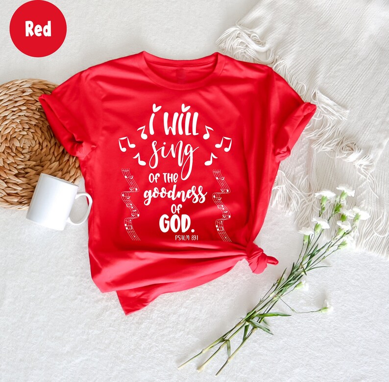 K&ouml;nnte beinhalten: Ein rotes T-Shirt mit dem wei&szlig;en Text "I will sing of the goodness of GOD", Noten und Notenlinien. Das T-Shirt ist am Saum geknotet. Eine wei&szlig;e Tasse und Blumen sind im Hintergrund.