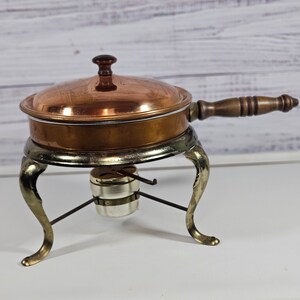 May include: A copper chafing dish with a wooden handle and a silver stand with three legs. The chafing dish has a lid with a knob on top.