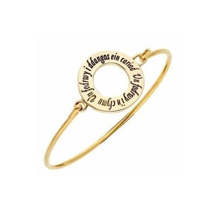 May include: A gold bangle bracelet with a circular charm that has the Welsh phrase "Yn fyd i'n gyd yn ein cariad" engraved around the edge.