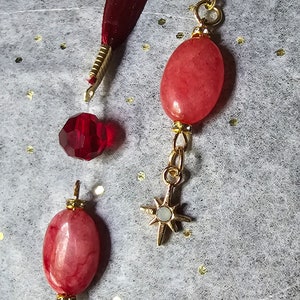 May include: Two red and white stone beads with gold accents and star charms hanging from a red ribbon.