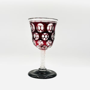 Può includere: Un calice da vino in vetro rosso con un design chiaro e a motivi. Il calice ha una coppa rotonda e uno stelo attorcigliato.