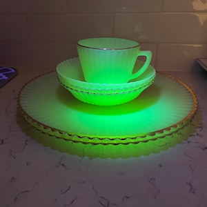 Op de afbeelding: Een set van vier gloeiende geelgroene glazen schalen met een gouden rand. De set bevat een kopje, een schoteltje en twee borden.