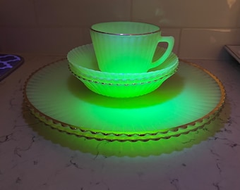 May include: A set of four glowing yellow-green glass dishes with a gold rim. The set includes a cup, a saucer, and two plates.
